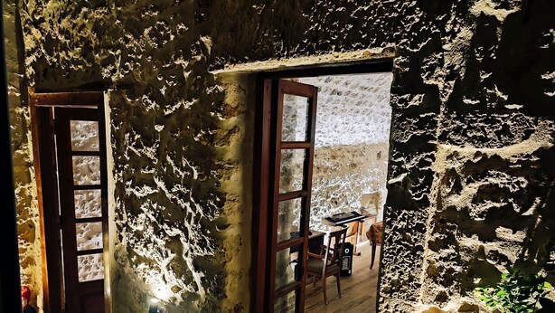 A rustic stone interior with a wooden door, a window, and a table with chairs.