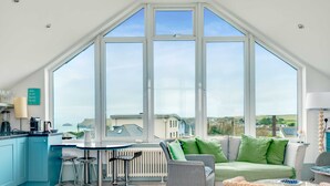A bright kitchen with a large bay window, a dining area, and a cozy seating space with a view of the countryside. - The Point (Wadebridge)