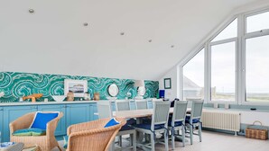 A dining area with wicker chairs and a table, a kitchen with teal patterned backsplash, and large windows offering a view. - The Point (Wadebridge)