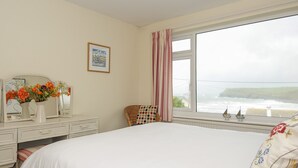 Ein Schlafzimmer mit einem großen Bett, einem Schminktisch, einem Spiegel und einem Fenster mit Blick auf das Meer.