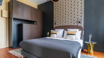 Een moderne slaapkamer met een groot bed, een donker houten kast, behang met een patroon en een klein rond tafeltje met een vaas.