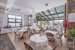 Enjoy meals in a well-lit dining area with large windows and a glass ceiling, surrounded by wicker chairs and framed menus.