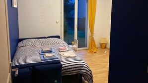 A bedroom with a bed, a window with yellow curtains, a small table with a lamp, and a view of the outdoors. - Family home 2 steps from Arradon center, Gulf and beaches (Arradon)