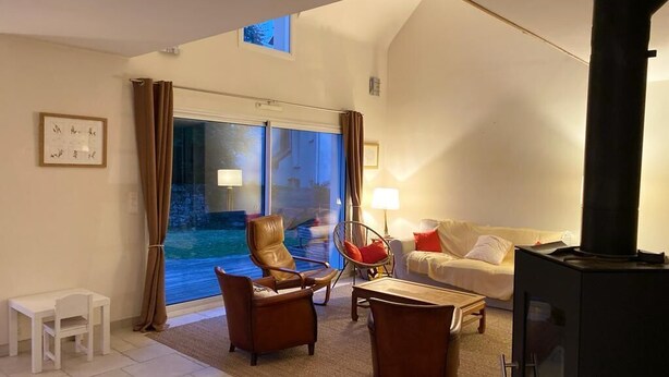 A living room with a fireplace, a sofa, a coffee table, and a chair. There is a window with curtains and a view of the outside. - Family home 2 steps from Arradon center, Gulf and beaches (Arradon)