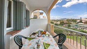 A balcony with a table set for a meal, featuring a view of a pool and buildings in the background. - Il Vecchio Faro A30 150m From The Beach (Loiri Porto San Paolo)