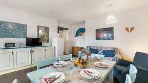A compact kitchen with a dining area, featuring a microwave, a flat-screen TV, and a dining table set for four. - Il Vecchio Faro A30 150m From The Beach (Loiri Porto San Paolo)