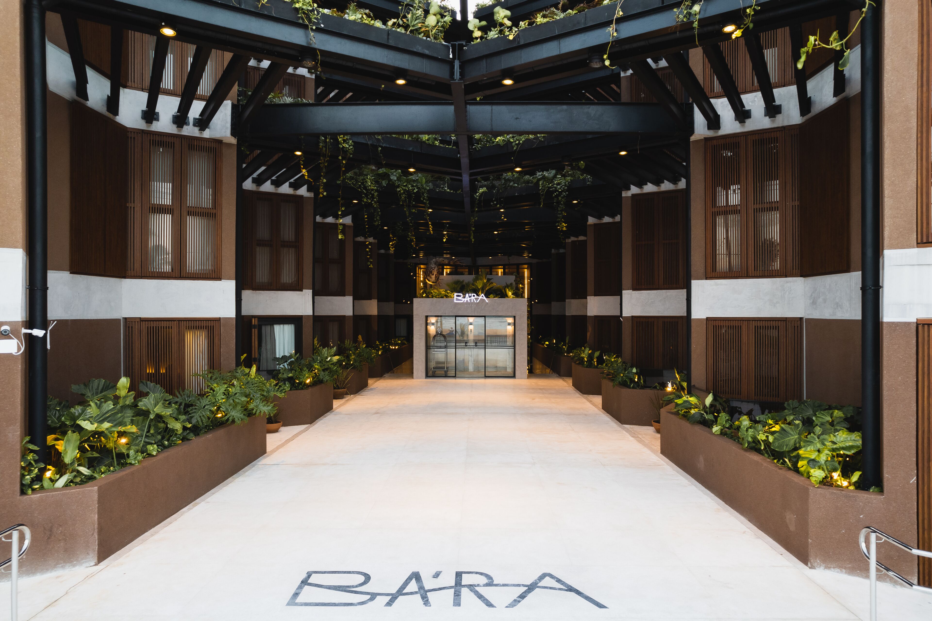 Entrada de un hotel con un corredor cubierto, detalles de madera y un letrero que dice "BARÁ".
