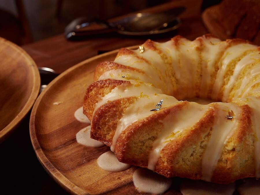 Un pastel Bundt con cobertura blanca sobre un plato de madera.