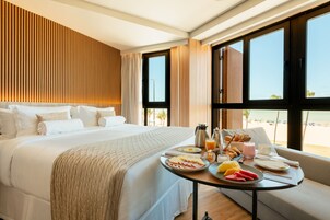 Camera d'albergo con un letto grande, un tavolo per la colazione con diversi cibi e vista sulla spiaggia.