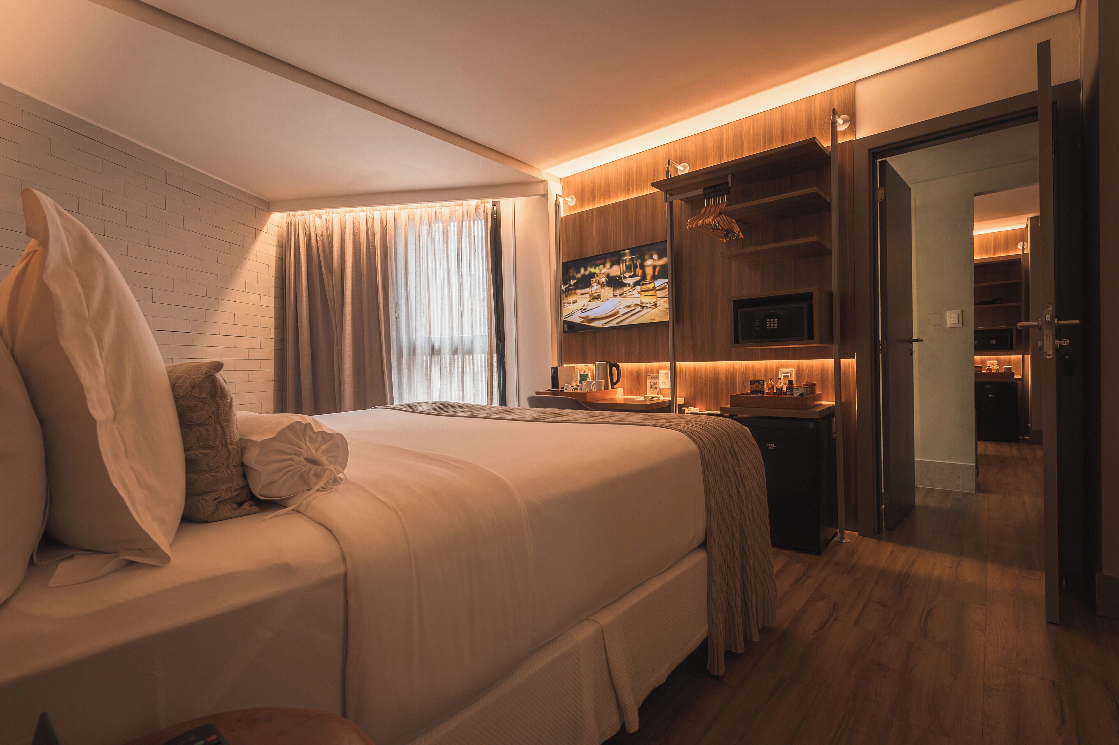 A modern hotel room with a large bed, a TV, a microwave, and a kitchenette.