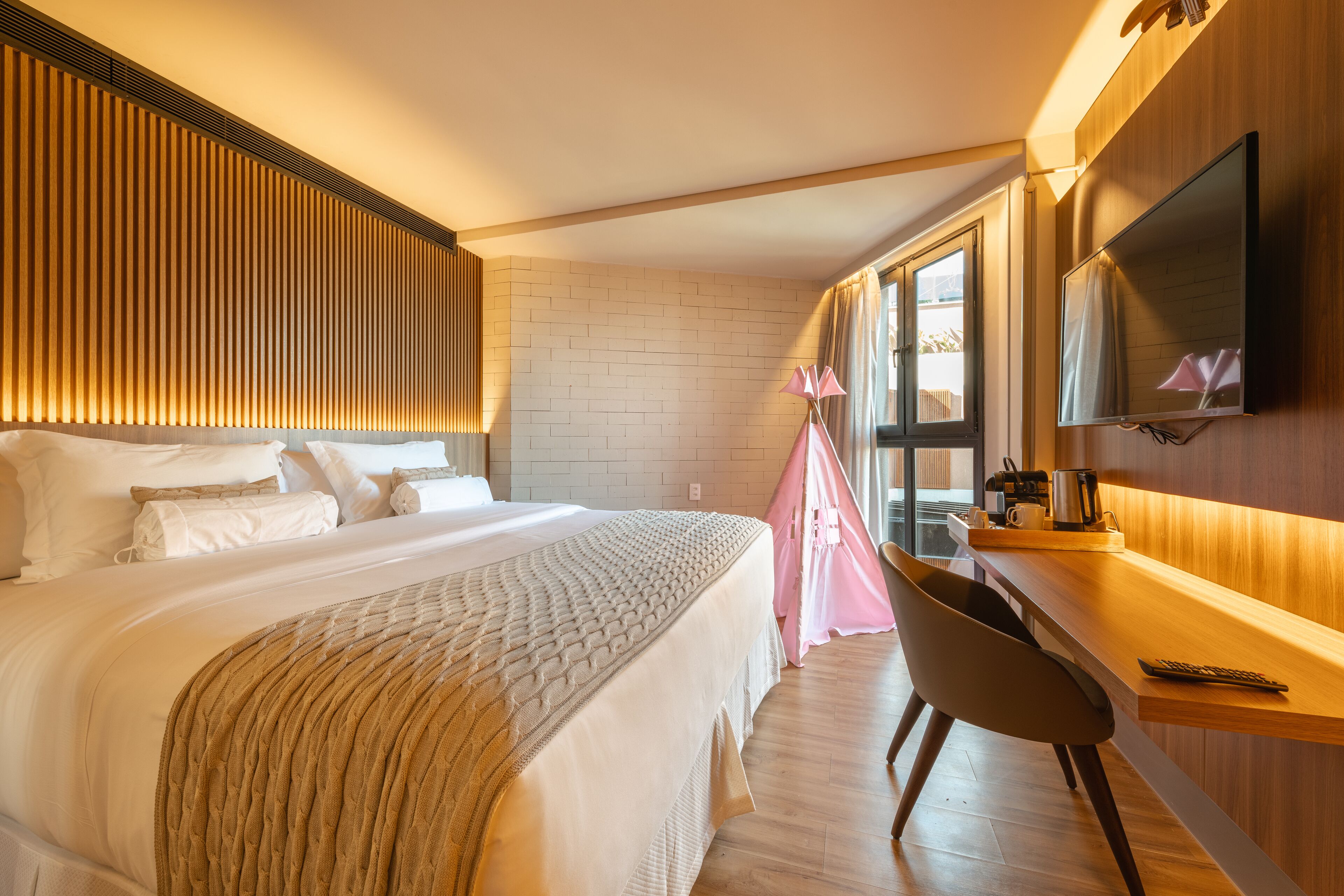 A modern hotel room with a large bed, a desk, a flat-screen TV, and a window with curtains.
