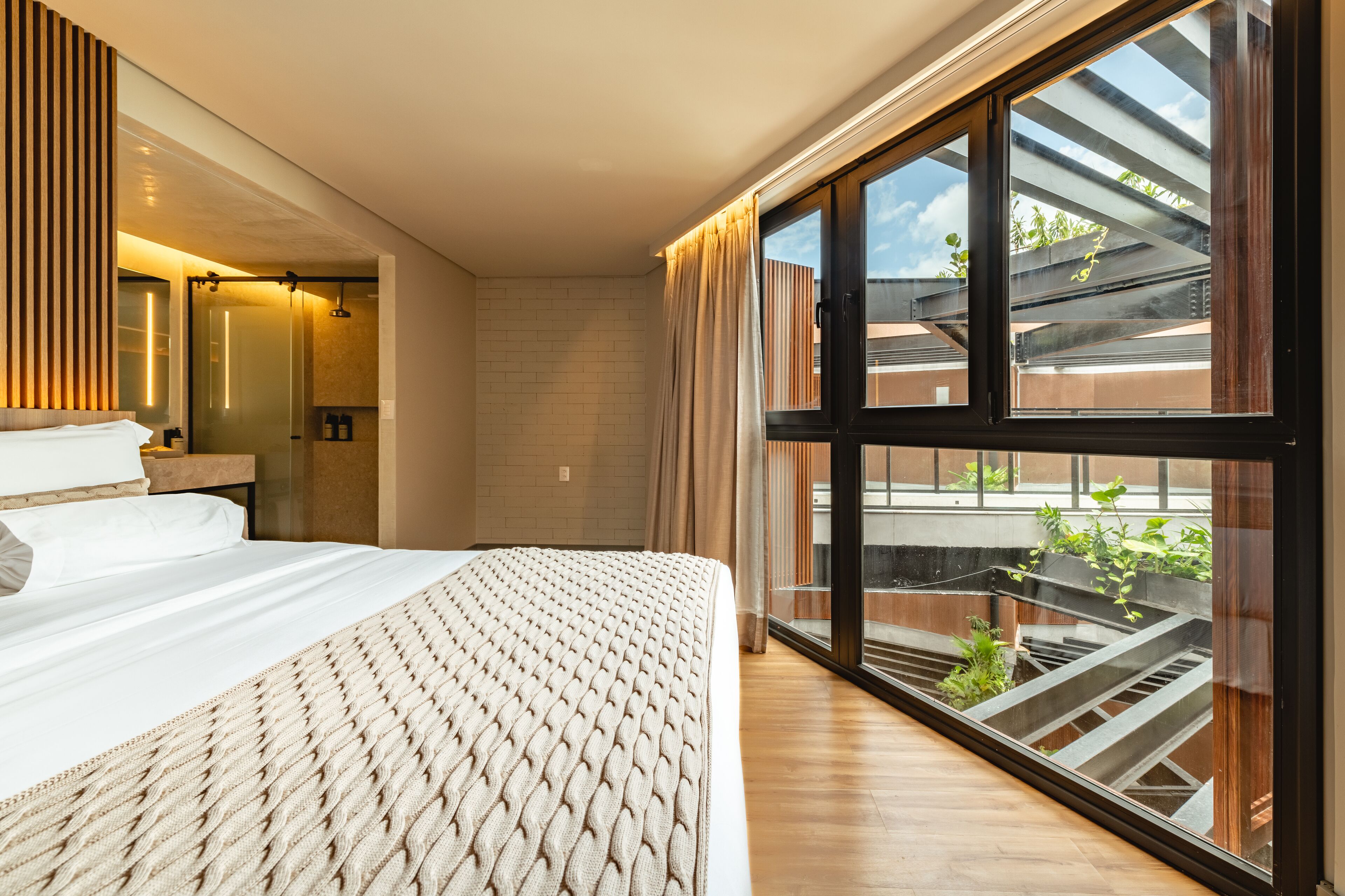 Un dormitorio moderno con una cama grande, un ventanal de vidrio que da a un balcón y vistas al exterior.