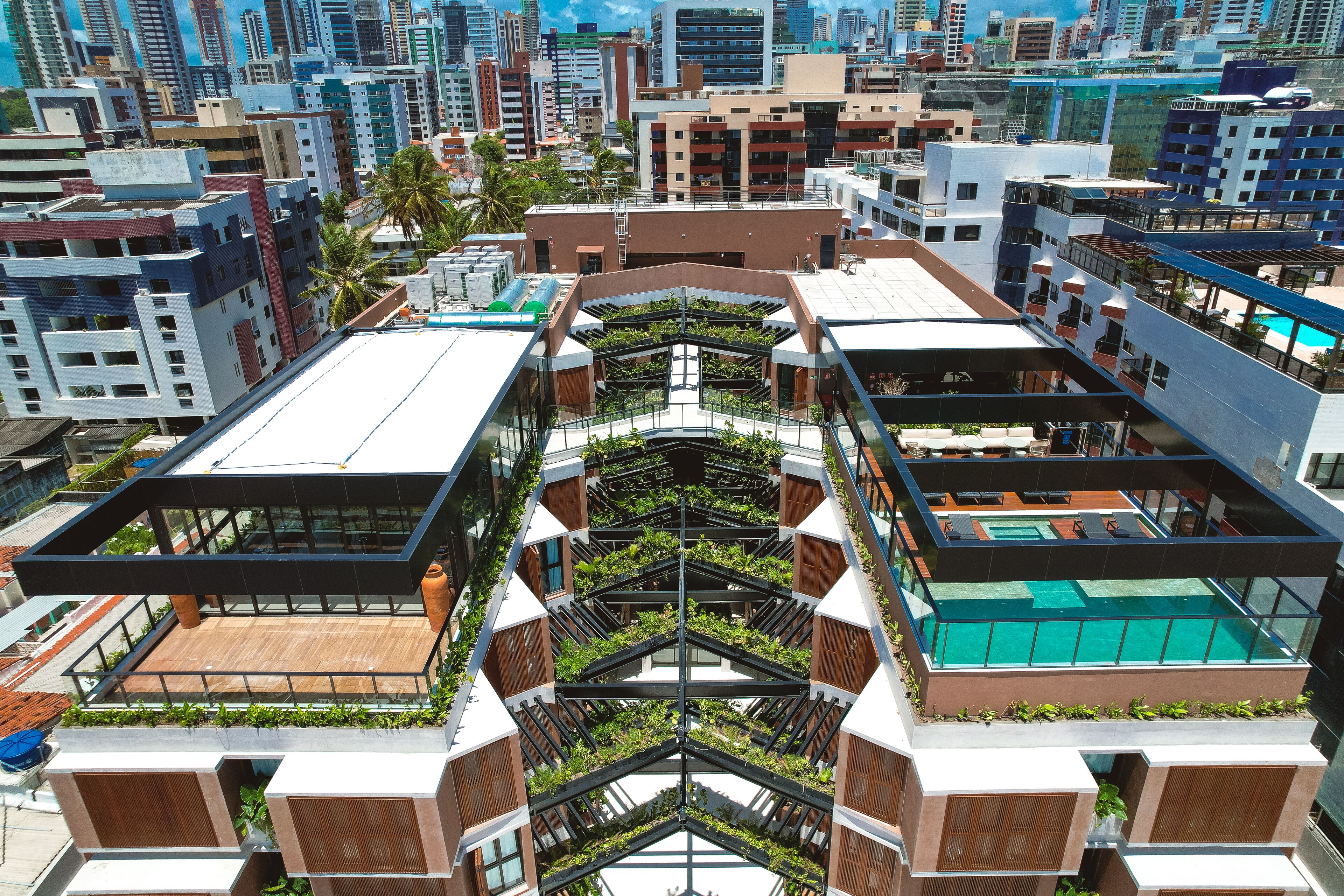 Un edificio moderno con varios balcones, una piscina en la azotea y un atrio central con plantas.