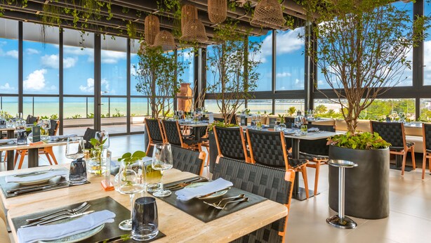Un restaurante con mesas preparadas para comer, ventanas amplias y vista al océano.