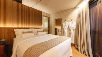 Una habitación de hotel con una cama grande, cabecera de madera, un espejo, bata y ventana con cortinas.