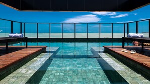 Una piscina infinita moderna con agua azul cristalina, terraza de madera y vista al océano.