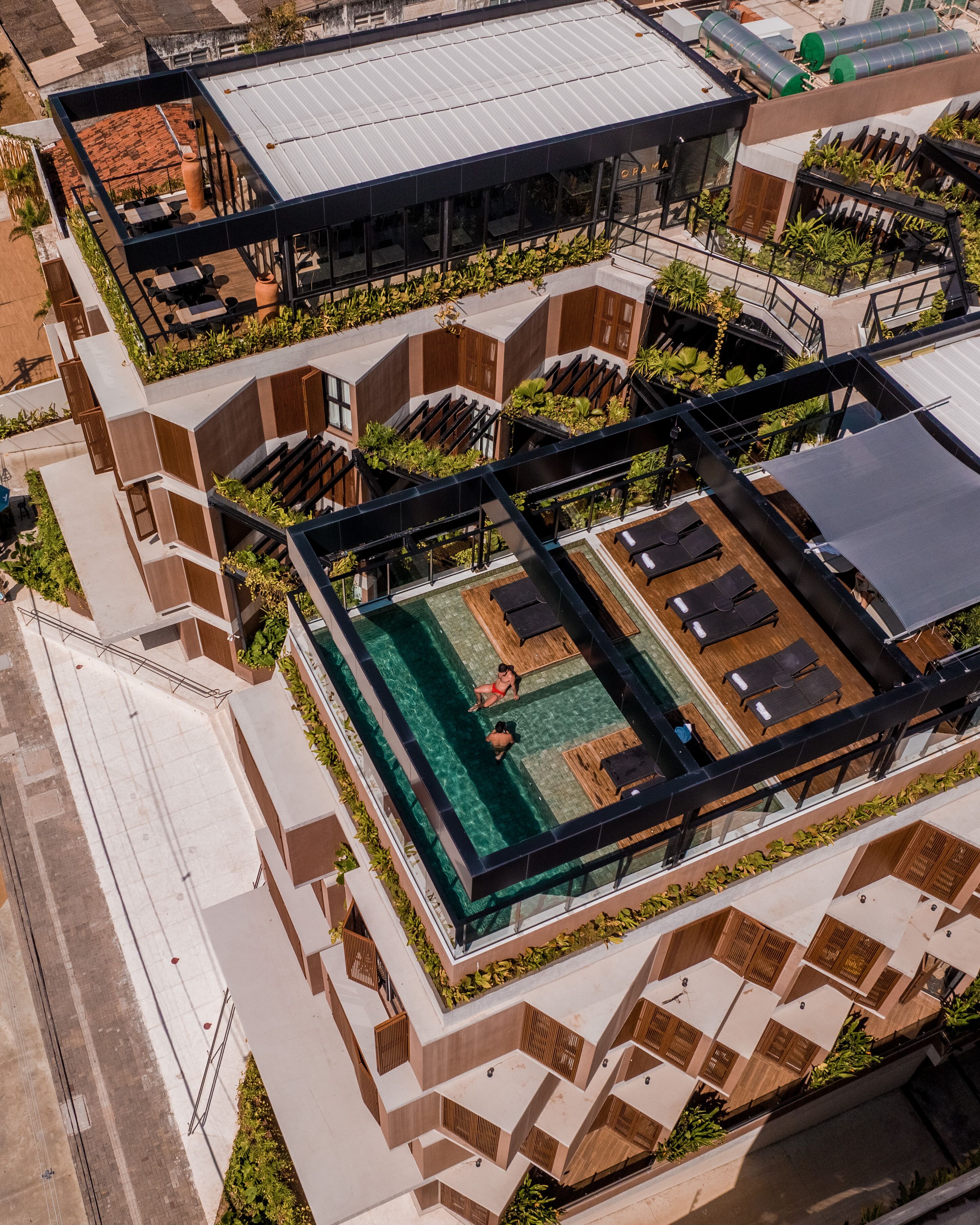 Vista aérea de um edifício moderno com piscina no terraço, áreas de estar ao ar livre e um pátio coberto.