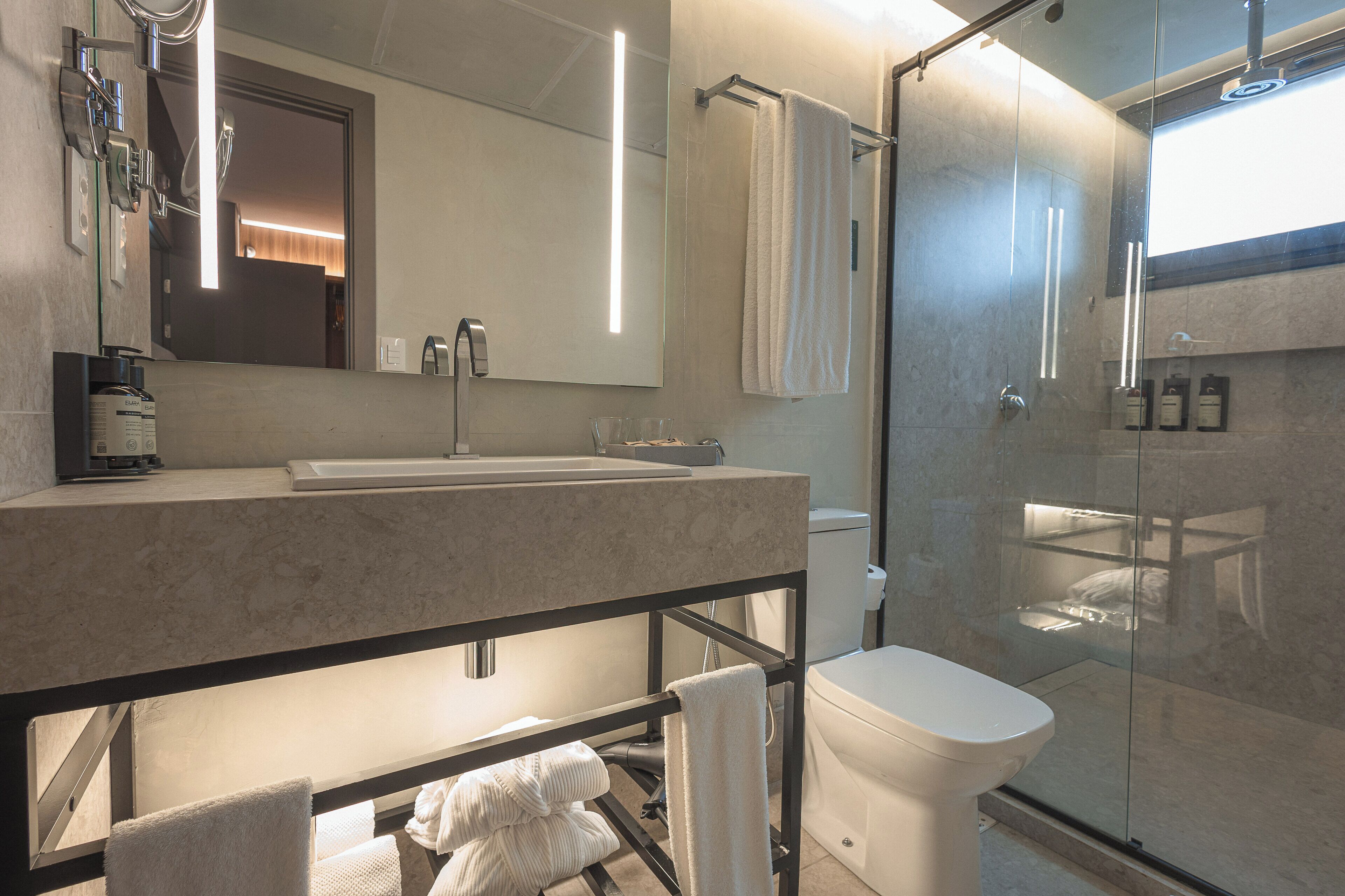 Un baño moderno con cabina de ducha de vidrio, un espejo grande y un lavamanos con toallero.