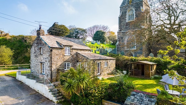 Une maison en pierre avec un petit jardin et une église en arrière-plan.