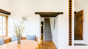 Un coin repas avec une table et des chaises en bois, un vase orné de branches et un escalier menant à une autre pièce.