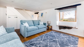 Un salon avec un canapé bleu, un fauteuil assorti, un plancher en bois, un tapis bleu, une fenêtre donnant sur un beau paysage et un escalier.