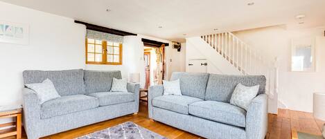 A spacious living room with two grey sofas, a wooden floor, and a staircase leading to another level.