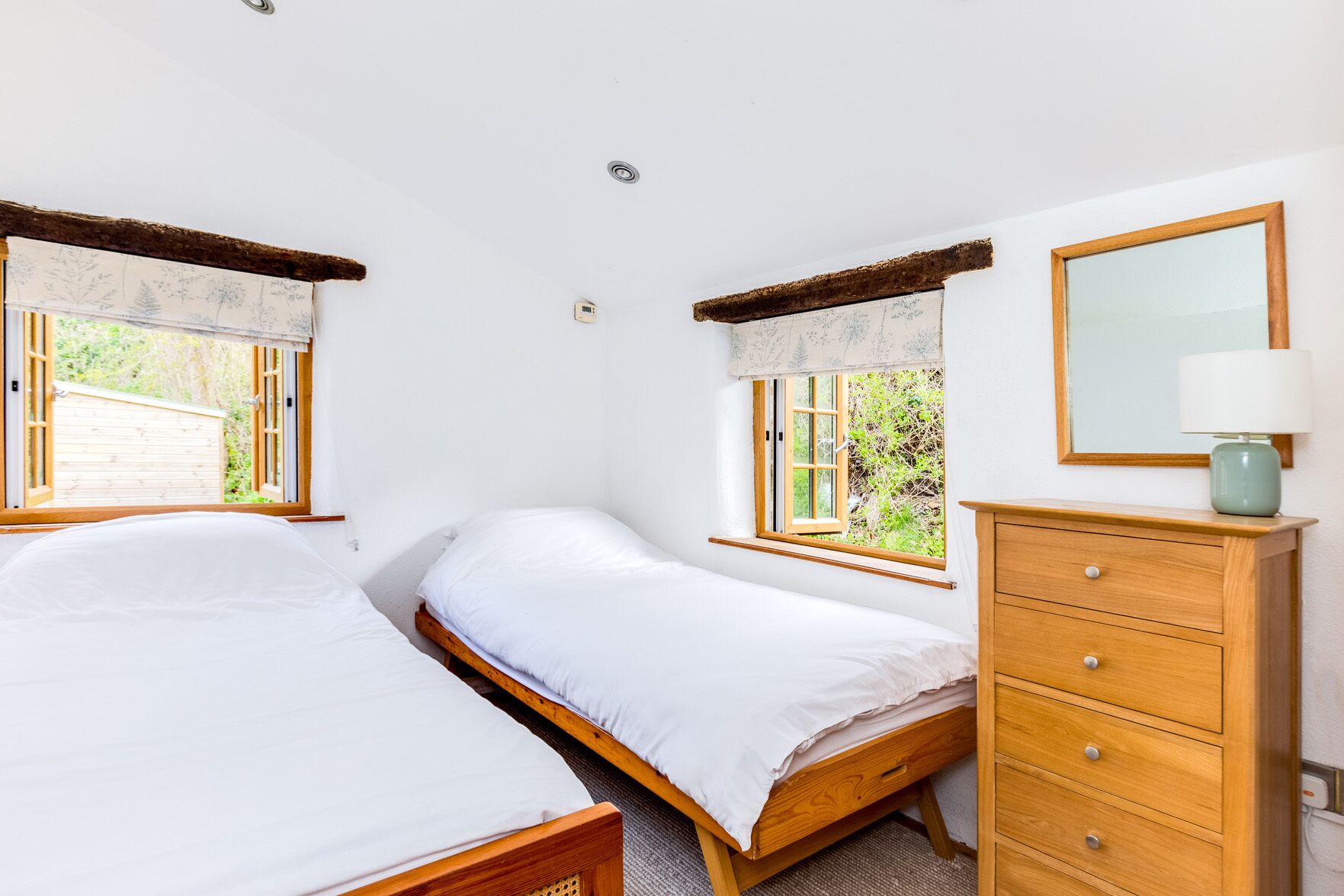 Un dormitorio con dos camas individuales, un aparador de madera, un espejo y una ventana con vistas a la vegetación.