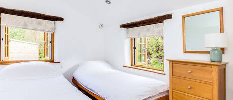 A bedroom with two single beds, a wooden dresser, a mirror, and a window with a view of greenery.