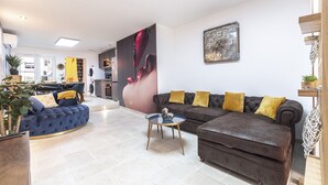 A modern living room with a blue sofa, a brown sofa, and a glass coffee table. There is a large wall clock and a potted plant. - LOFT with private jacuzzi, CENTRE VILLE PONTOISE (Pontoise)