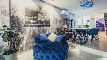 Ein modernes Wohnzimmer mit einem blauen, gesteppten Sofa, einem Fahrrad und einem Essbereich mit Tisch und Stühlen.