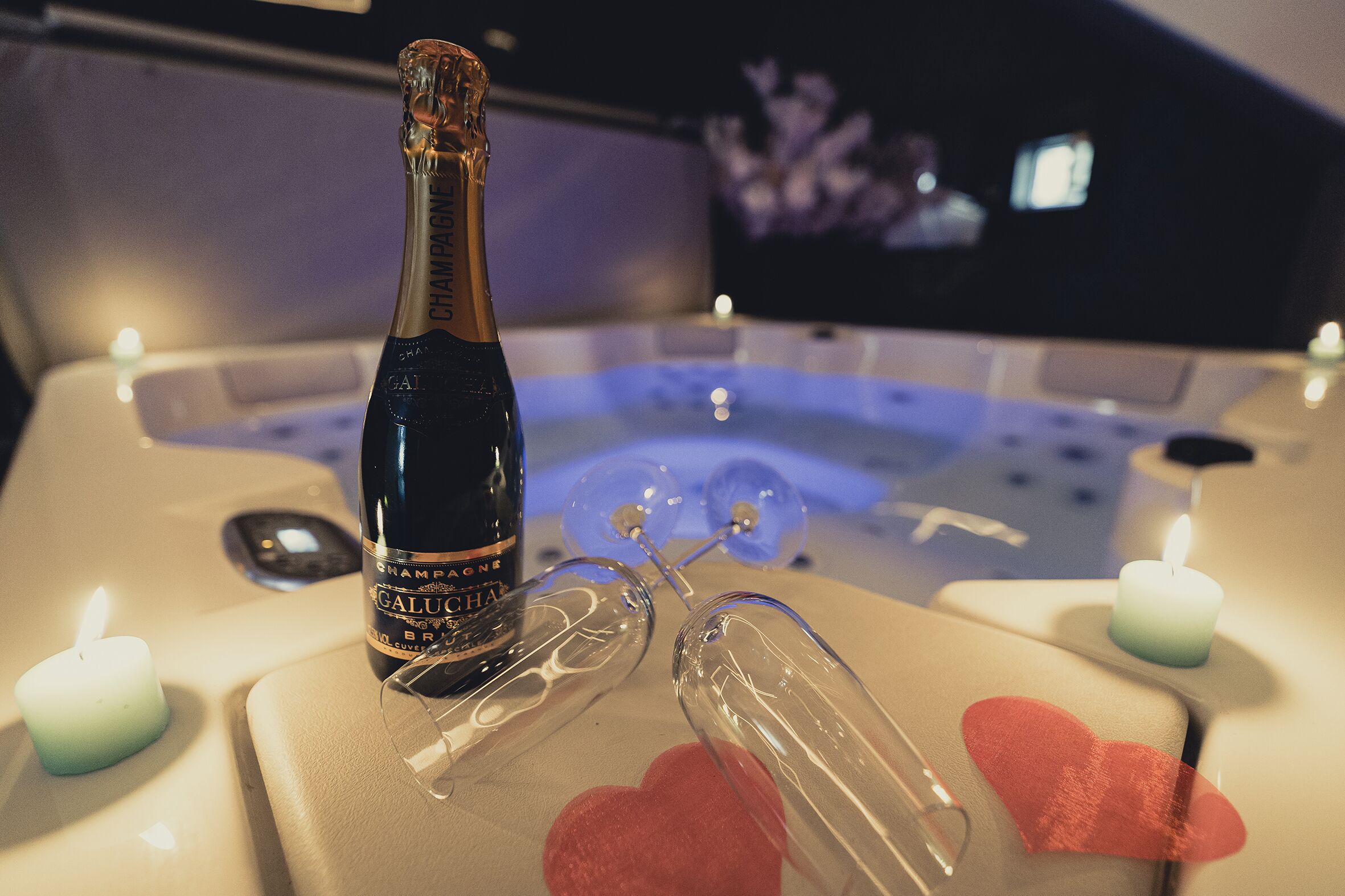 A bottle of champagne, glasses, and candles on a table in a room with a bathtub.