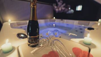 A bottle of champagne, glasses, and candles on a table in a room with a bathtub.