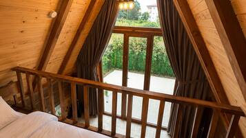 A bedroom with a wooden ceiling, a bed, a balcony with curtains, and a hanging light fixture.