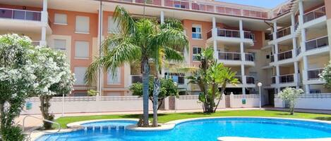 Ein mehrstöckiges Hotel mit Pool, umgeben von Palmen und einem gepflegten Rasen.