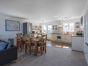 A modern kitchen with white cabinets, a dining area with wooden chairs, and a large map on the wall. - Sea View Apartment in centre of Rhosneigr - Pass the Keys (Rhosneigr)