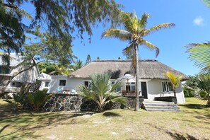 Ein Haus mit Strohdach, einer Steinmauer, einer Palme und einem Rasen.