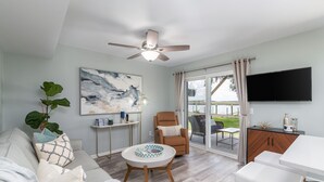 Una sala de estar moderna con ventilador de techo, un ventanal con cortinas, un televisor de pantalla plana y una zona de comedor.