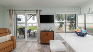 Una sala moderna con un sofá, un armario de madera, un televisor y una zona de cocina con encimera y cesta de frutas.