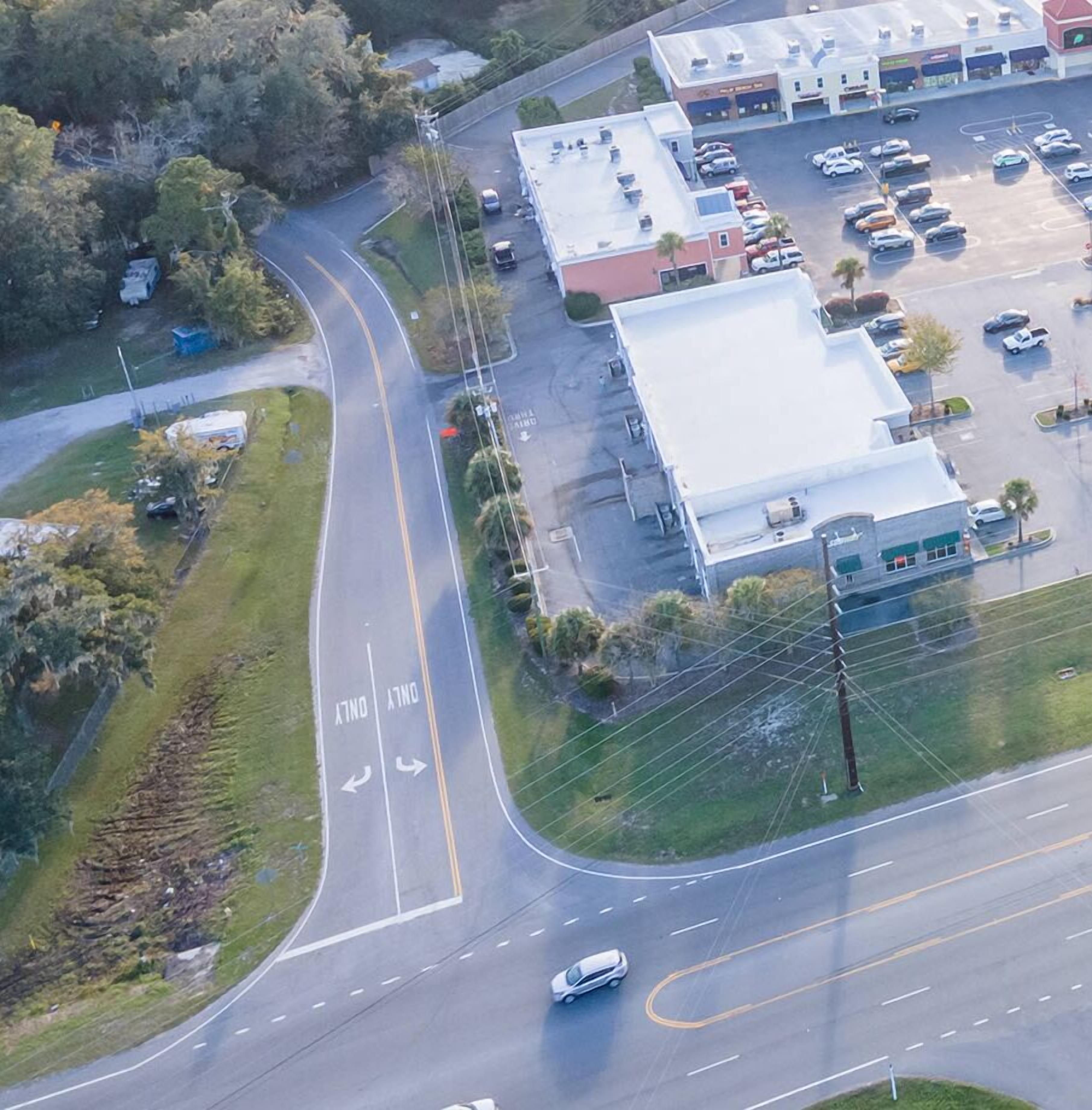 Vista aérea de una zona comercial con un estacionamiento, una calle con un carril 'DUTY ONLY', y un edificio de techo plano.