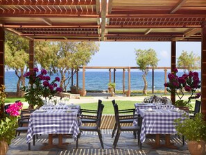 Enjoy al fresco dining with a view of the sea from this outdoor dining area, featuring two tables set with tablecloths and comfortable seating.