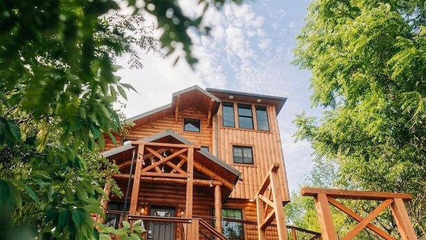 Une cabane en bois à plusieurs niveaux, avec un escalier menant à l’étage supérieur, entourée d’arbres.