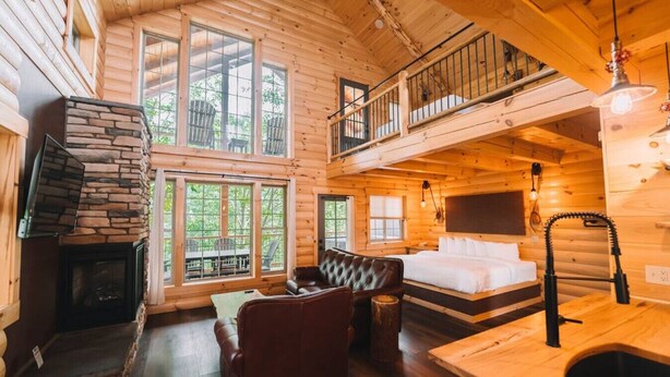 L’intérieur d’une cabane en rondins, avec une cheminée en pierre, un canapé, un lit et un balcon.