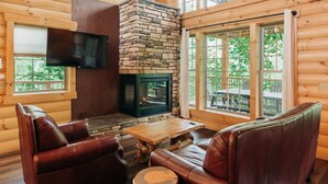 Un intérieur de chalet chaleureux avec une cheminée en pierre, des canapés en cuir et une table basse en bois.