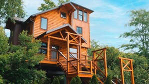 Une cabane en bois à plusieurs niveaux, dotée d’un balcon et d’un escalier.