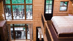 Une cabane en rondins avec une chambre à coucher à l’étage, un balcon avec des chaises et une vue sur la forêt environnante.