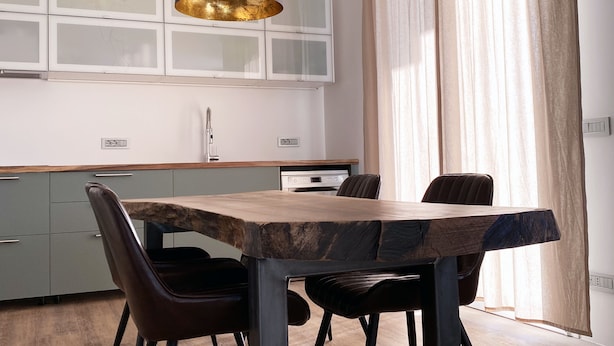 En matplats med ett träbord och fyra stolar, en modern hänglampa och ett kök i bakgrunden.