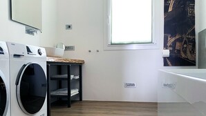 Ett tvättrum med en tvättmaskin, ett torkställ, ett fönster och en spegel som är monterad på väggen.