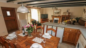 A dining area with a wooden table set for four, a vase with flowers, and a television in the background. - Y Cartws (Llandysul)