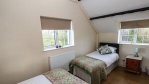 A bedroom with two beds, a nightstand, a lamp, and a window with a view of greenery. - Y Cartws (Llandysul)
