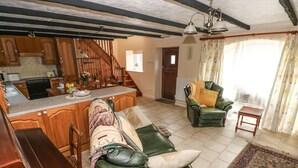 A spacious living area with a green leather sofa, a wooden coffee table, and a green armchair. A kitchen with wooden cabinets and a built-in island is visible in the background. - Y Cartws (Llandysul)